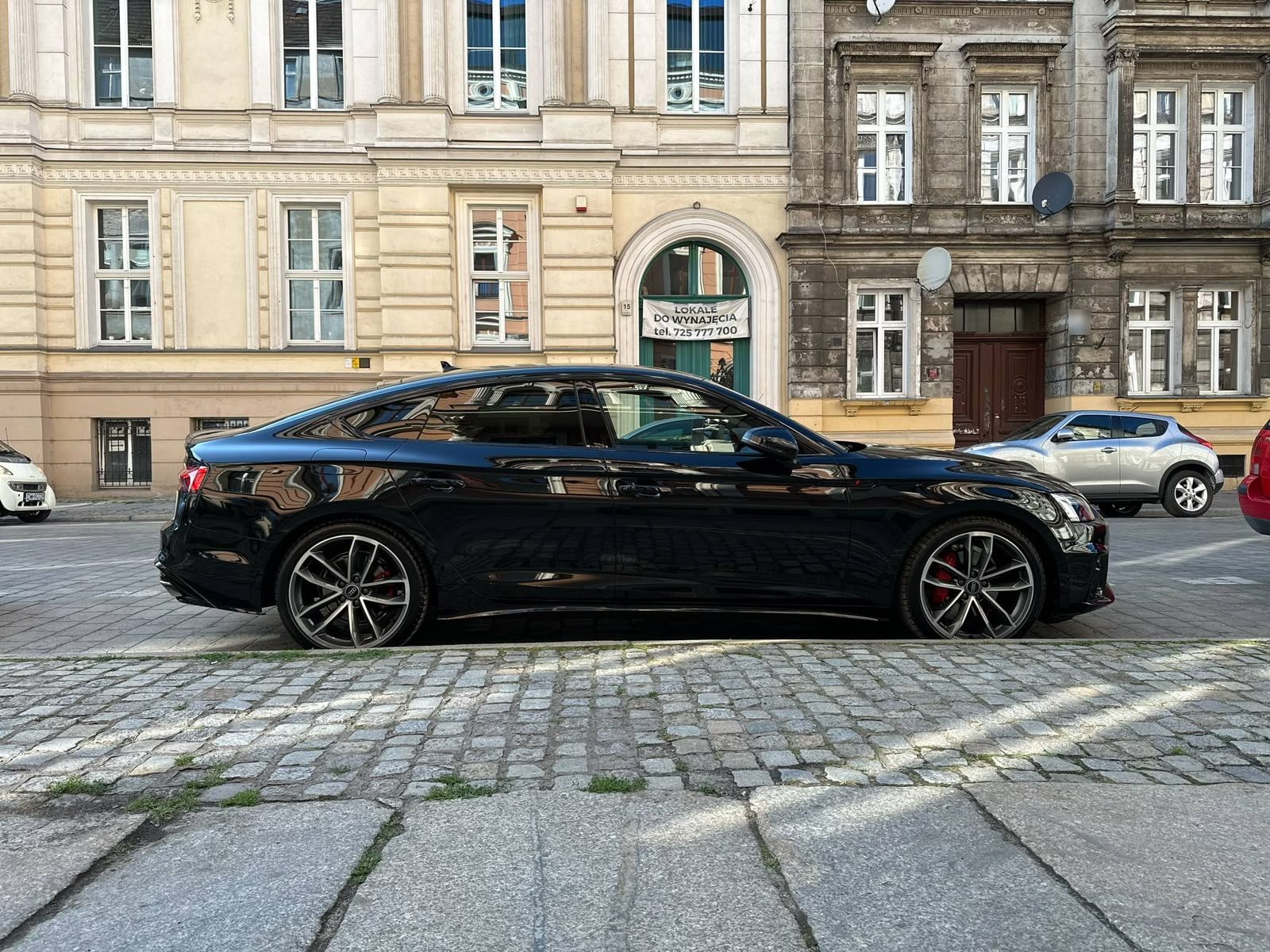 Czarne Audi A5 Sportback z boku, na brukowanej ulicy przy kamienicach